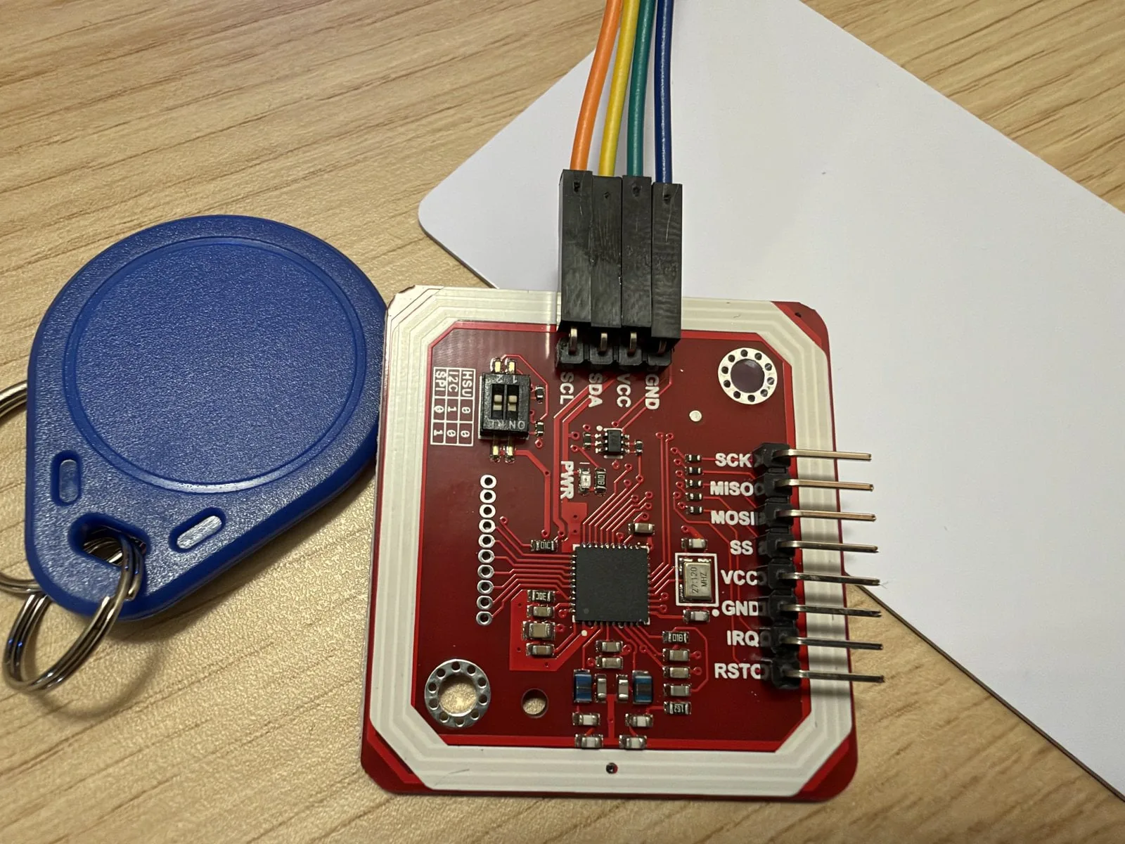 Módulo PN532 V3 rojo con sus pines rotulados para I²C y SPI, junto a un llavero NFC azul y una tarjeta blanca