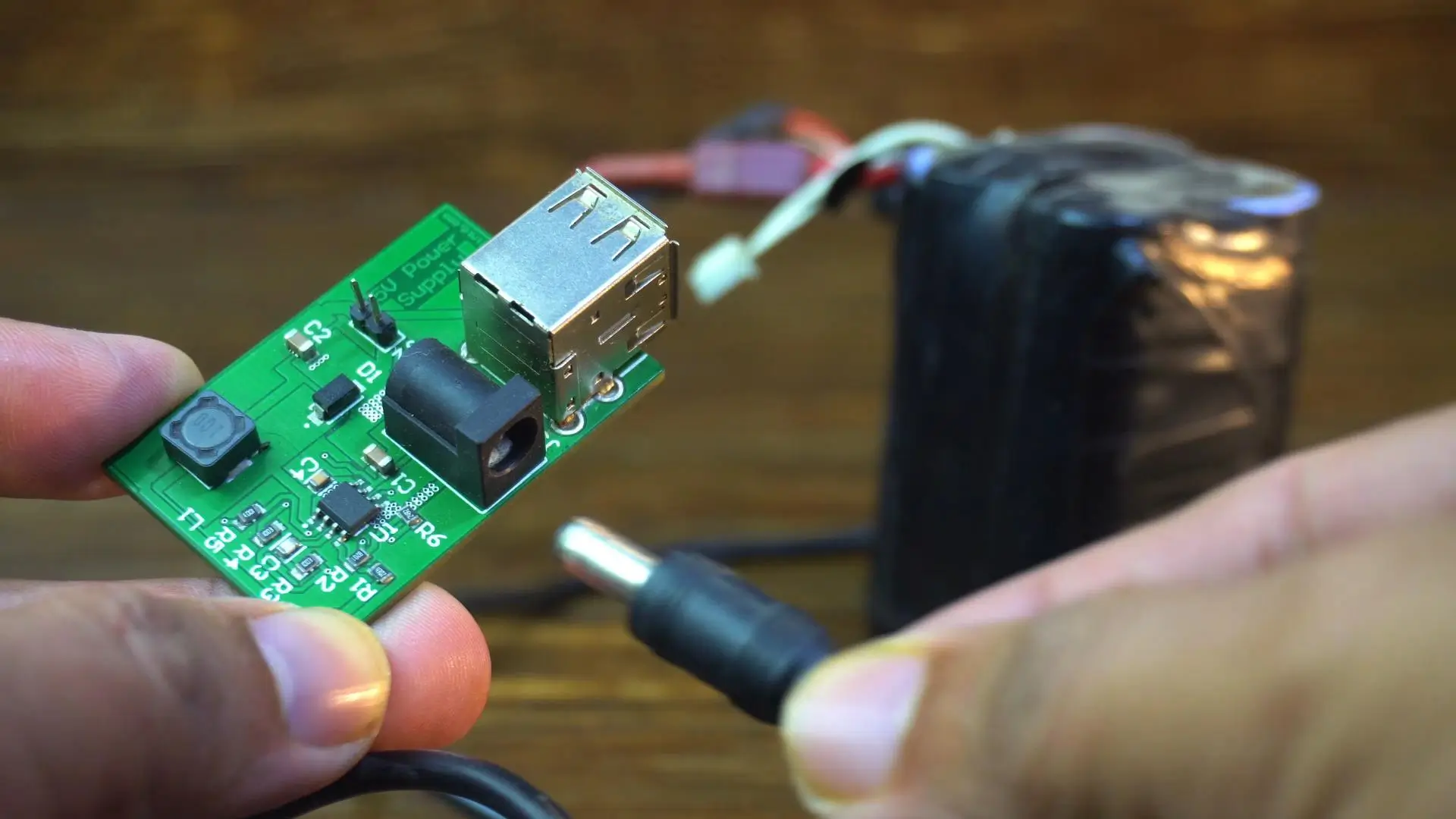 Módulo regulador de 5V/3A con salida USB sostenido en la mano y pack de batería 4S de litio al lado