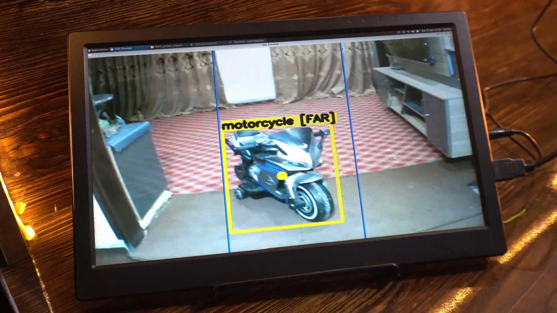Monitor mostrando la detección en vivo: una moto dentro de un recuadro amarillo etiquetado "motorcycle [FAR]", con la imagen dividida en tres zonas verticales