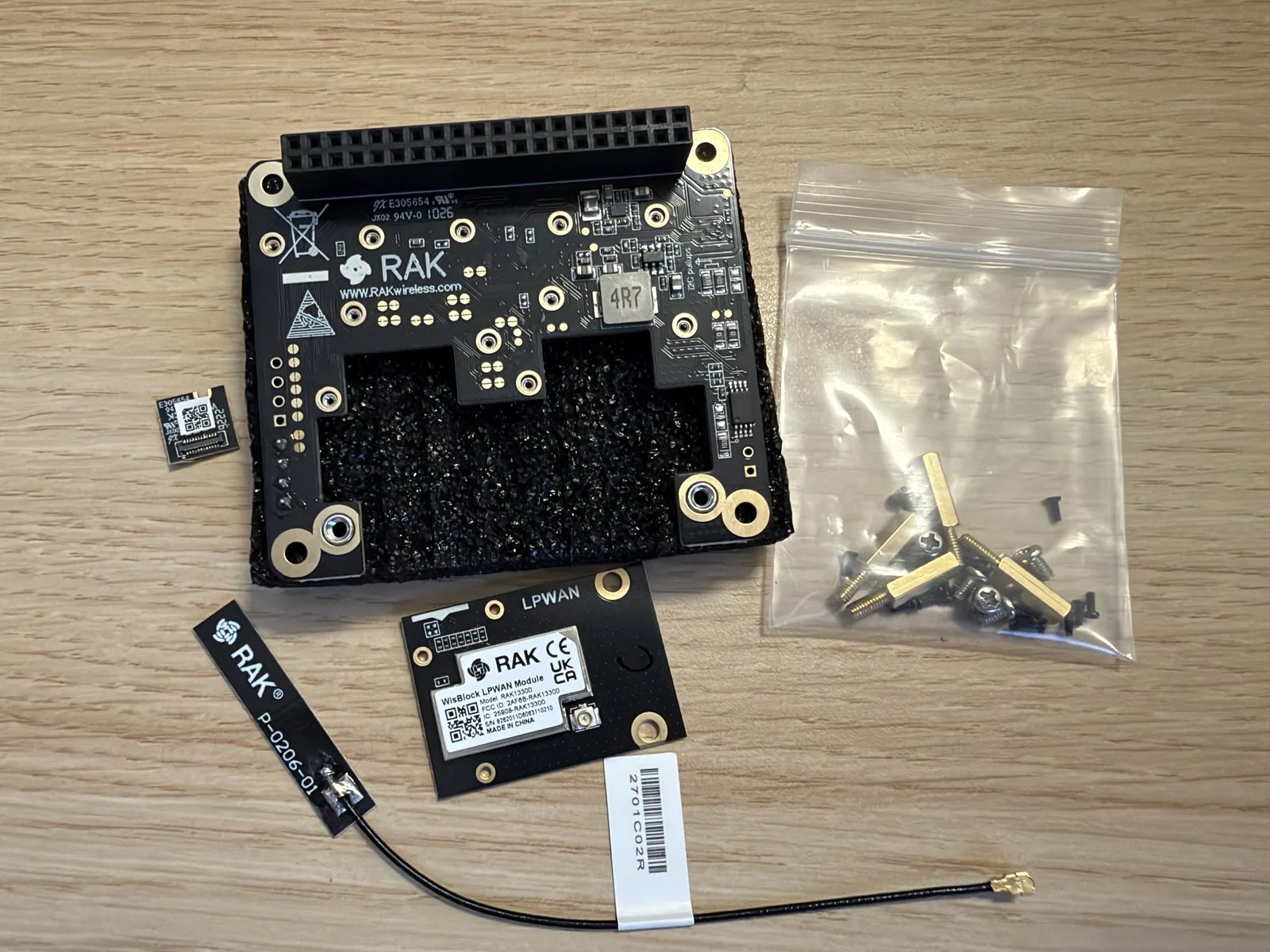 HAT RAK6421, módulo de radio RAK13300, sensor RAK1901, antena de PCB y bolsa de tornillos sobre una mesa de madera