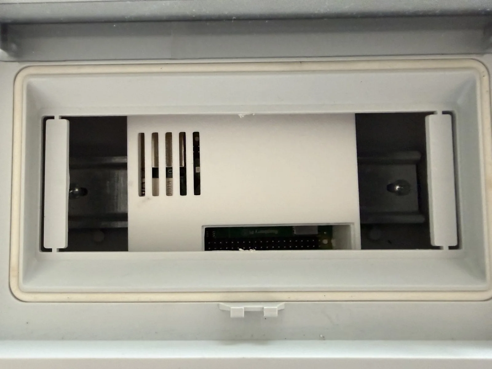 Tablero con la tapa embellecedora cerrada; en la ventana asoma el gabinete impreso con sus ranuras de ventilación y el campo GPIO abierto