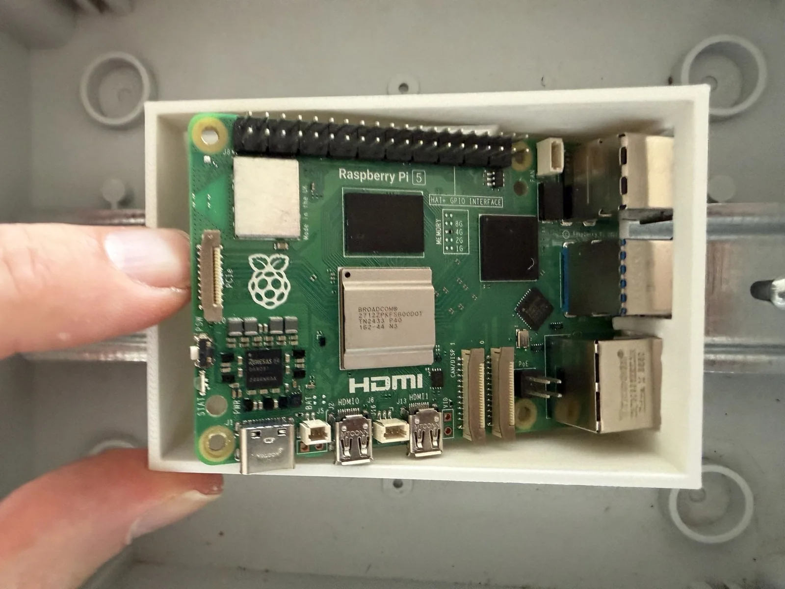 Una mano inserta un Raspberry Pi 5 inclinado en la bandeja impresa, con los conectores por delante