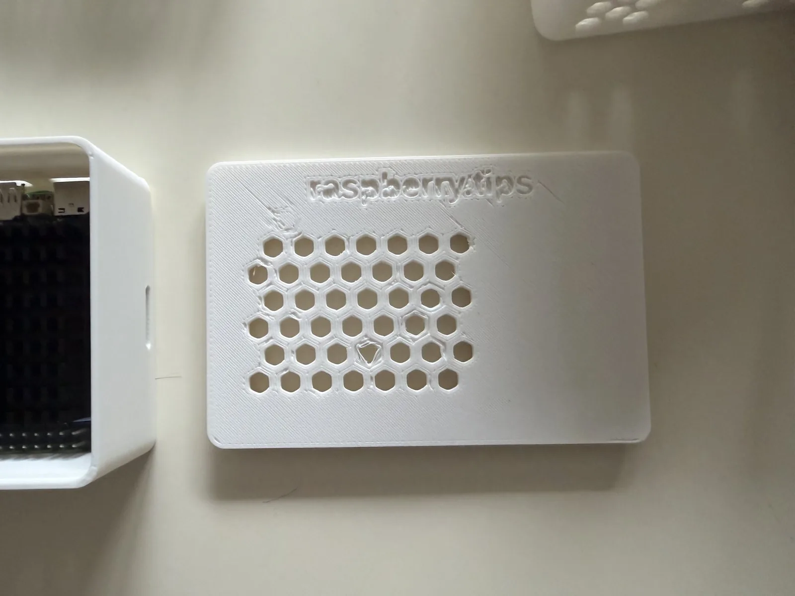 Tapa impresa con rejilla de panal y logotipo en relieve, junto a la bandeja con el Raspberry Pi montado