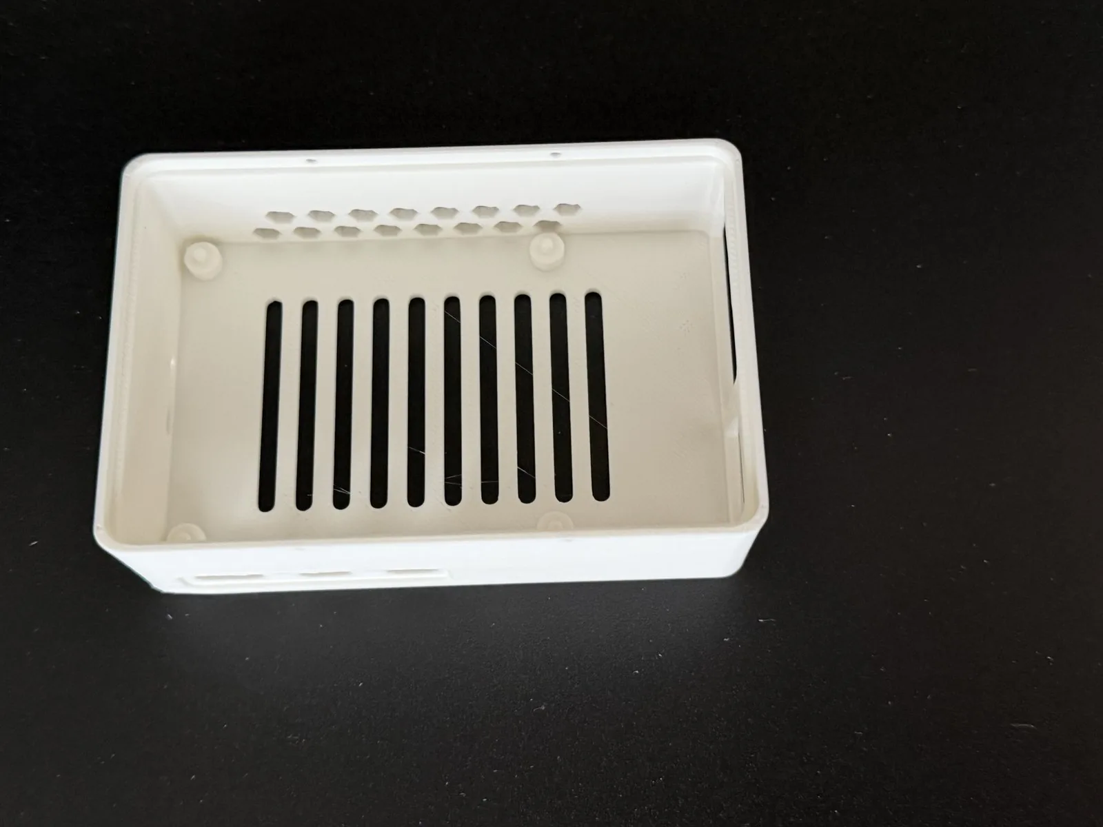 Bandeja vacía impresa en PLA blanco con ranuras en el piso, campo de panal en la pared del GPIO y cuatro postes de montaje con pivote