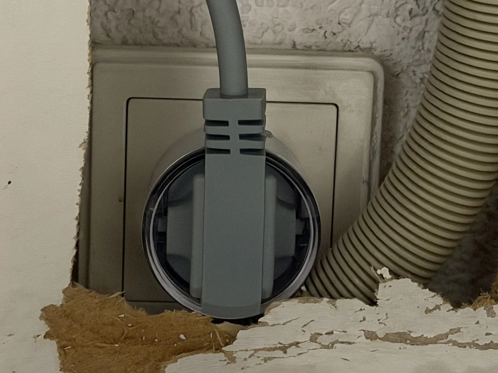 Enchufe inteligente instalado en el tomacorriente detrás del mueble de cocina, con el enchufe acodado del lavavajillas al frente y la manguera de desagüe al lado