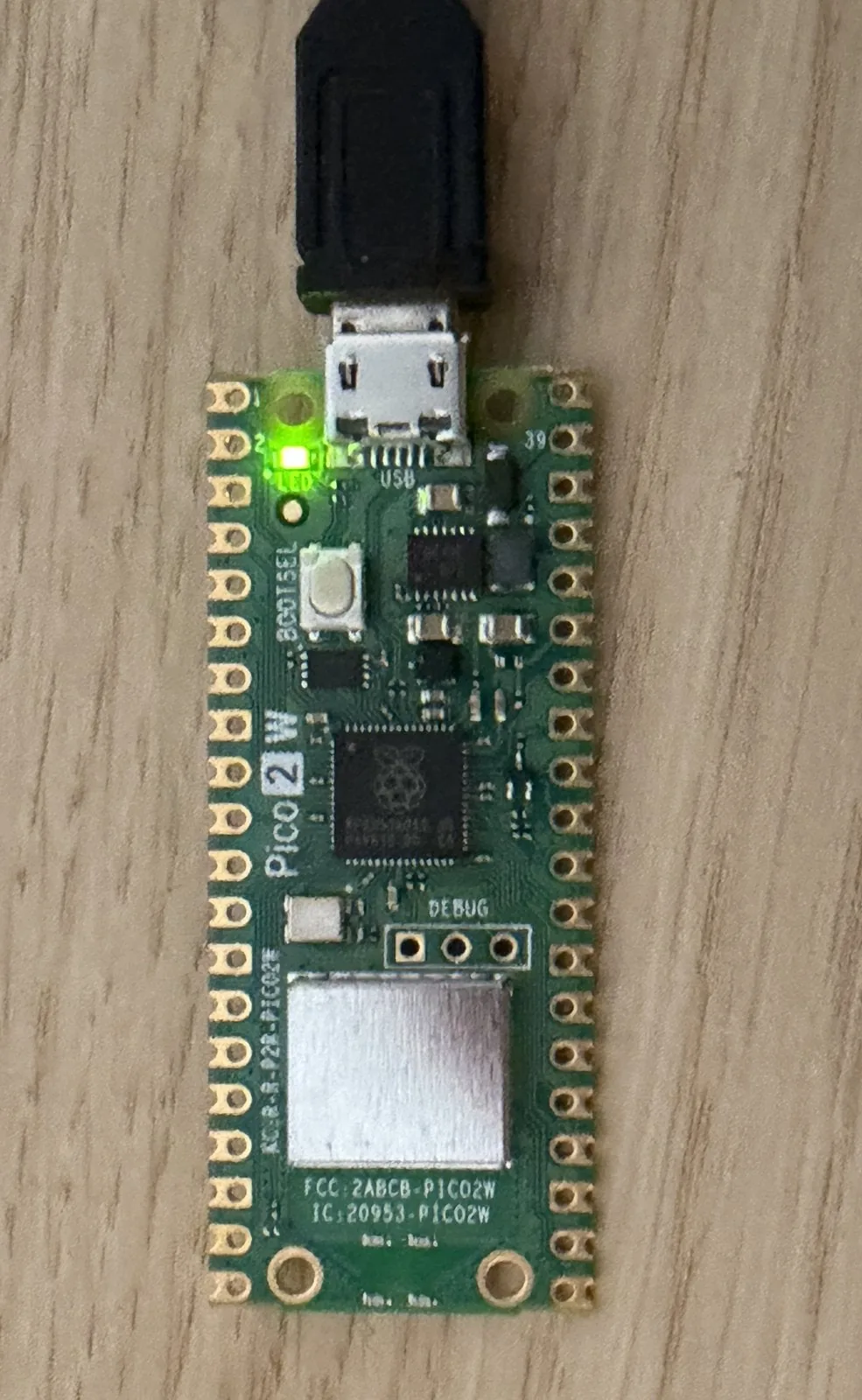 Pico 2 W sobre una mesa de madera con el LED verde integrado encendido junto al conector USB