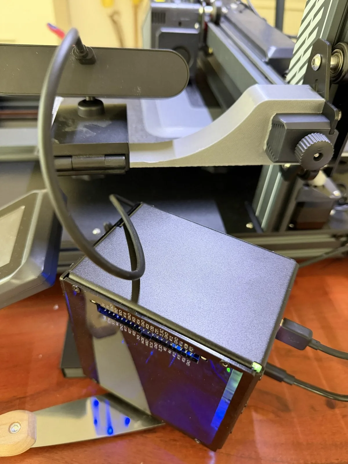 Raspberry Pi 5 en gabinete Pironman con la webcam sujeta con pinza, junto a la Elegoo Neptune 4 Plus