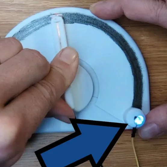 Mano barriendo el brazo del modelo sobre la pista de grafito con una flecha apuntando al LED que se enciende