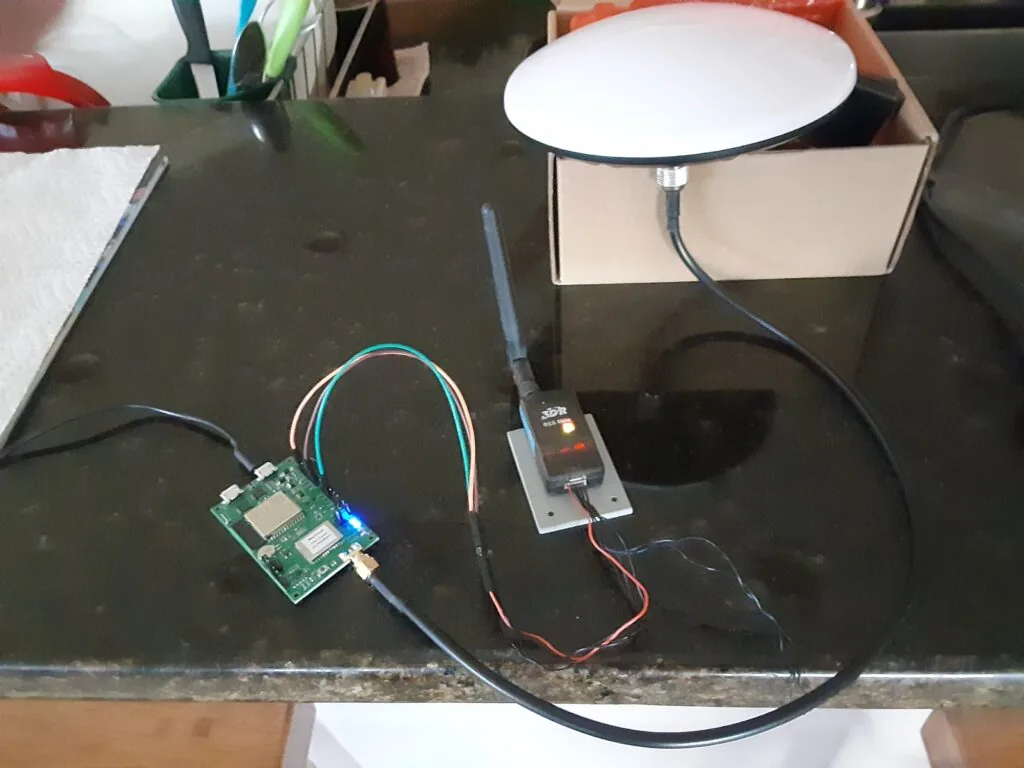 Prototipo de la estación base sobre el banco: placa PX1122R cableada a la radio SiK y a la antena domo de grado topográfico