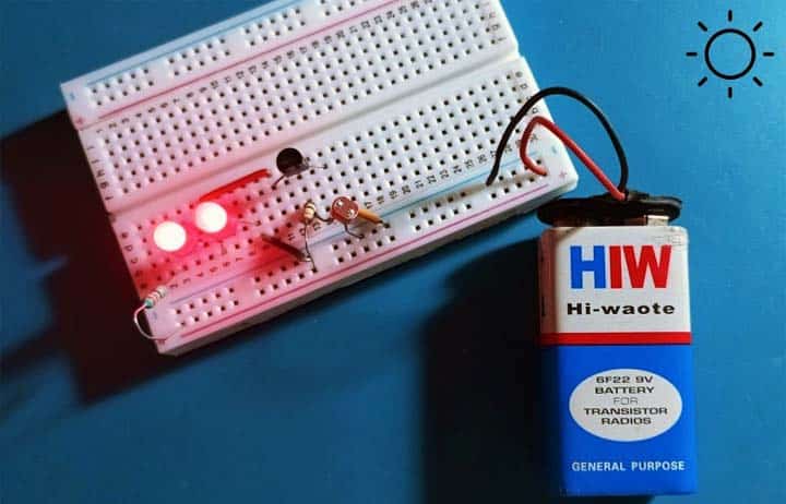 Montaje en protoboard con dos LED rojos encendidos y una pila de 9V, simulando el comportamiento de día