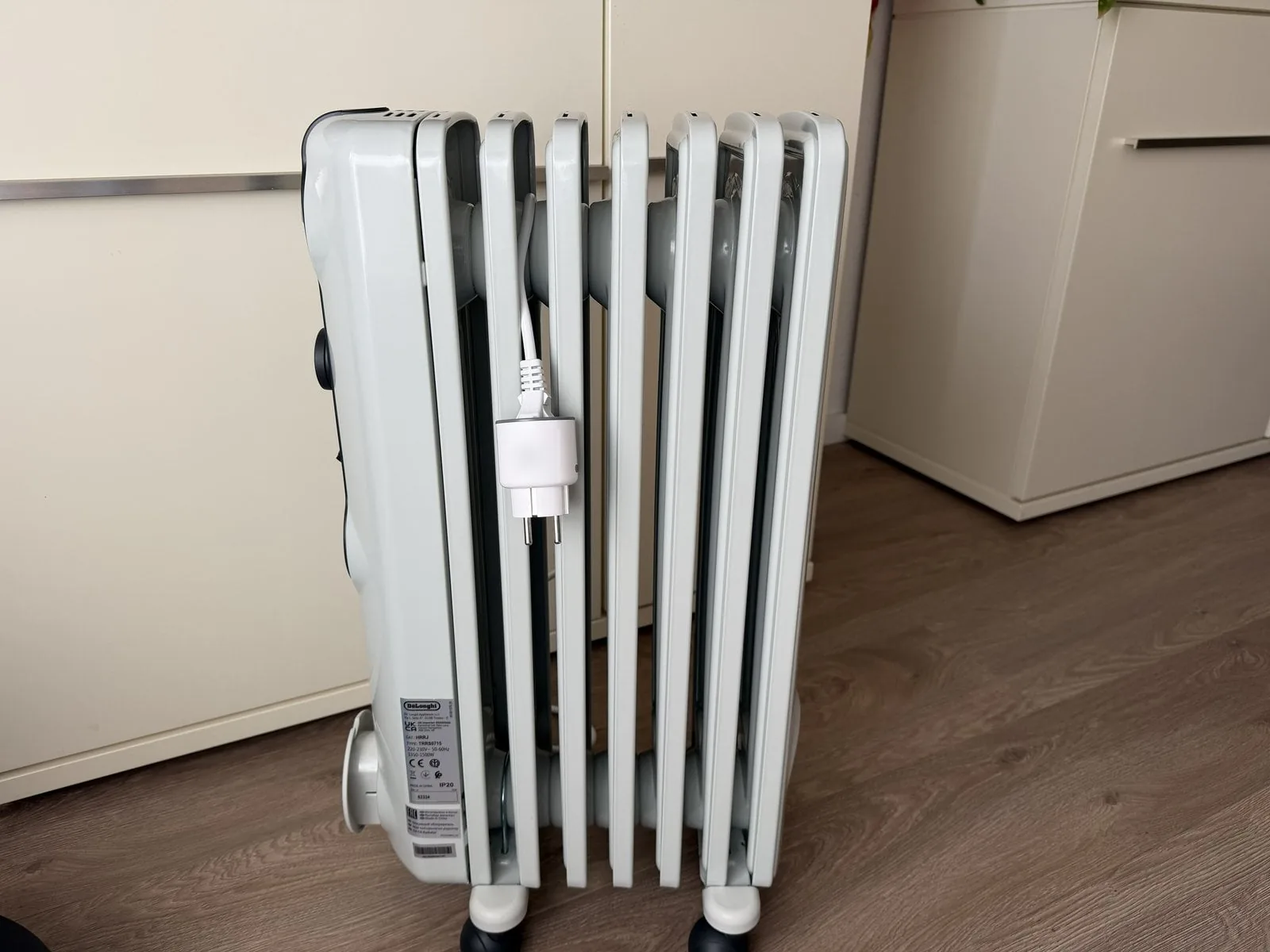 Estufa de aceite De'Longhi Radia S vista de costado junto al enchufe Zigbee SONOFF S60ZBTPF, con la placa que indica 1.350 a 1.500 W