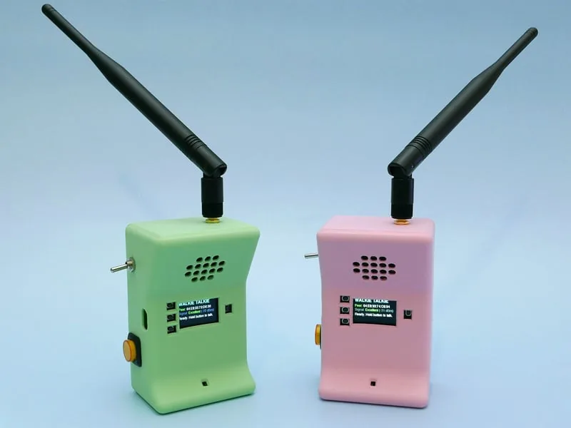 Par de walkie talkies terminados, en verde y rosado, con la antena puesta y la pantalla mostrando la interfaz WALKIE TALKIE